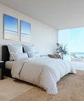 Ein großes, einladendes Doppelbett bezogen mit eleganter, weißer Microstripe Bettwäsche und mehreren Kissen in einem minimalistischen Schlafzimmer mit offener Fensterfront zum Meer