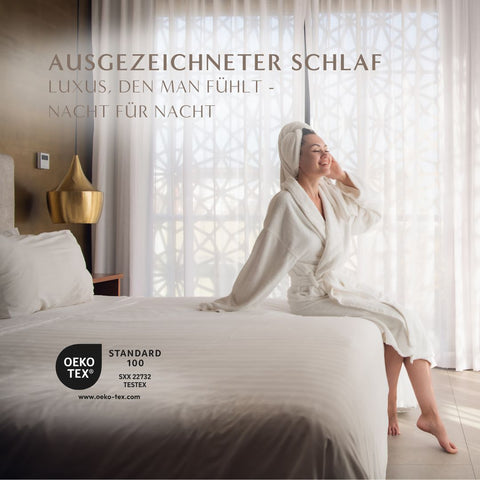 Frau im Bademantel genießt erholsamen Schlafkomfort mit OEKO-TEX zertifizierter Gänsedaunendecke im stilvollen Hotelzimmer