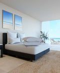 Modernes Schlafzimmer mit weißen Kissenschonbezügen auf einem eleganten Bett vor heller Fensterfront mit Meerblick