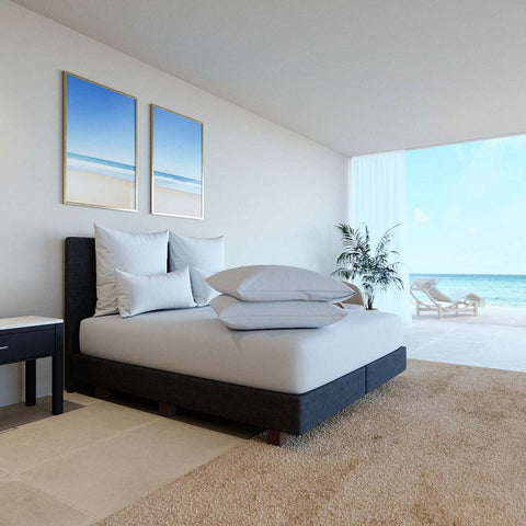 Modernes Schlafzimmer mit weißen Kissenschonbezügen auf einem eleganten Bett vor heller Fensterfront mit Meerblick