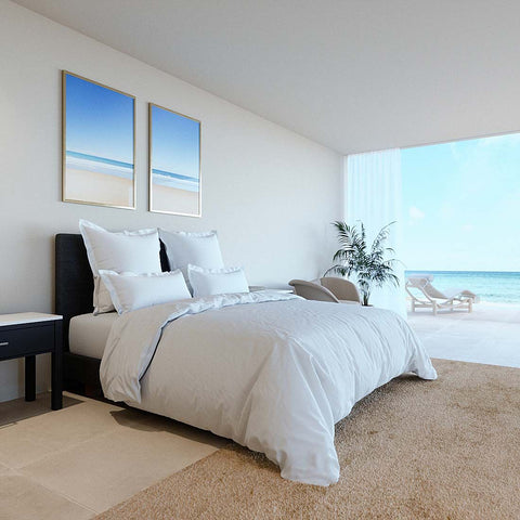 Modern eingerichtetes Schlafzimmer mit weißen Kopfkissenbezügen auf elegant bezogenem Bett und hellem Meerblick im Hintergrund
