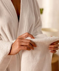 Person in einem Bademantel hält eine weiche weiße Badematte aus dem Premium Luxushotel Badematten 3er Set für ein komfortables Spa- und Hotelerlebnis.