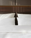 Nahaufnahme der ordentlich arrangierten weißen Kopfkissen auf einem Bett, bezogen mit glattem Premium Bettdeckenbezug vor einem strukturierten, gepolsterten Kopfteil in einem Hotelzimmer.