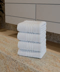 Premium Luxushotel-Handtücher 4er Set mit vier sauber gefalteten weißen Handtüchern auf einer Natursteinablage in einem modernen Badezimmer.